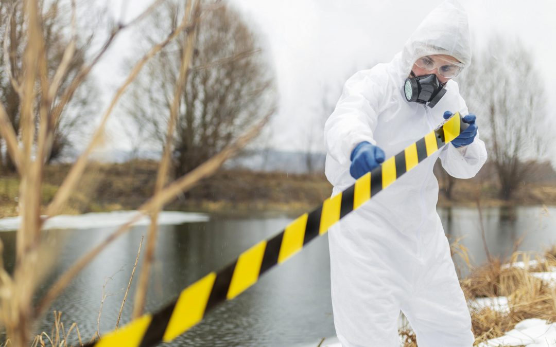 Tècnic amb vestit de protecció contra l’amiant inspeccionant una zona exterior contaminada amb cinta de seguretat.