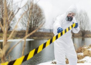 Tècnic amb vestit de protecció contra l’amiant inspeccionant una zona exterior contaminada amb cinta de seguretat.