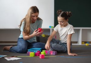 Psicóloga realizando una intervención terapéutica personalizada con una niña durante una sesión de apoyo para favorecer el desarrollo cognitivo, emocional y las funciones ejecutivas.