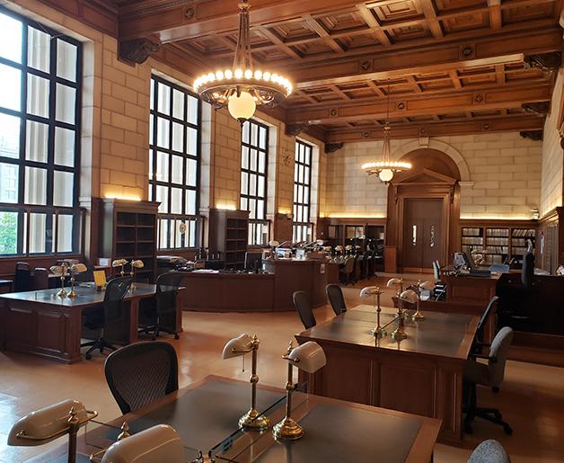 Spacious national library reading room featuring wooden study desks, vintage brass lamps, tall grid windows, and a coffered ceiling, showcasing spaces dedicated to preserving documentary heritage and linguistic diversity.